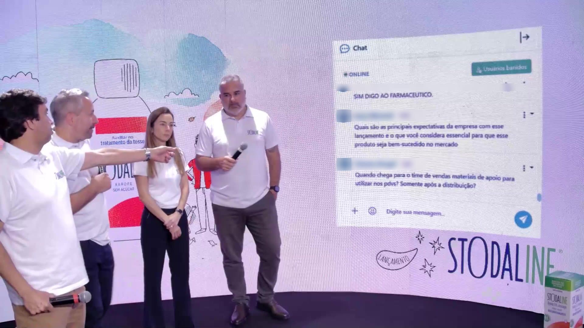 Apresentadores no estúdio apontando para o chat da live, exibido no painel de LED curvo atrás deles
