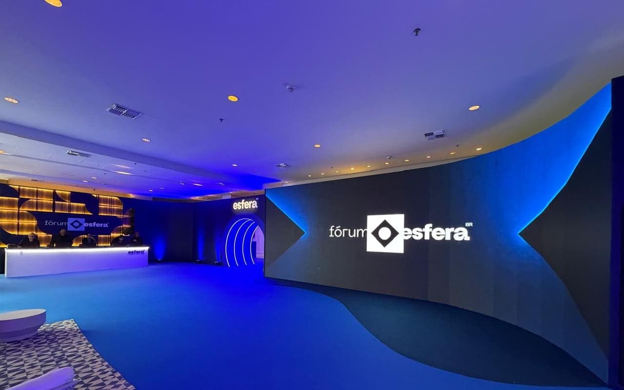 Foyer de evento com uma parede curva de LED exibindo a marca, arco iluminado ao fundo e luz azul de ambientação