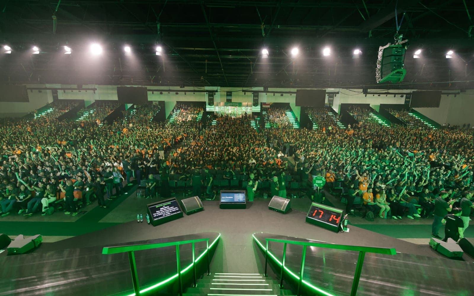Vista do palco para uma arena lotada, com caixas de retorno na boca de cena e line array suspenso sobre a plateia