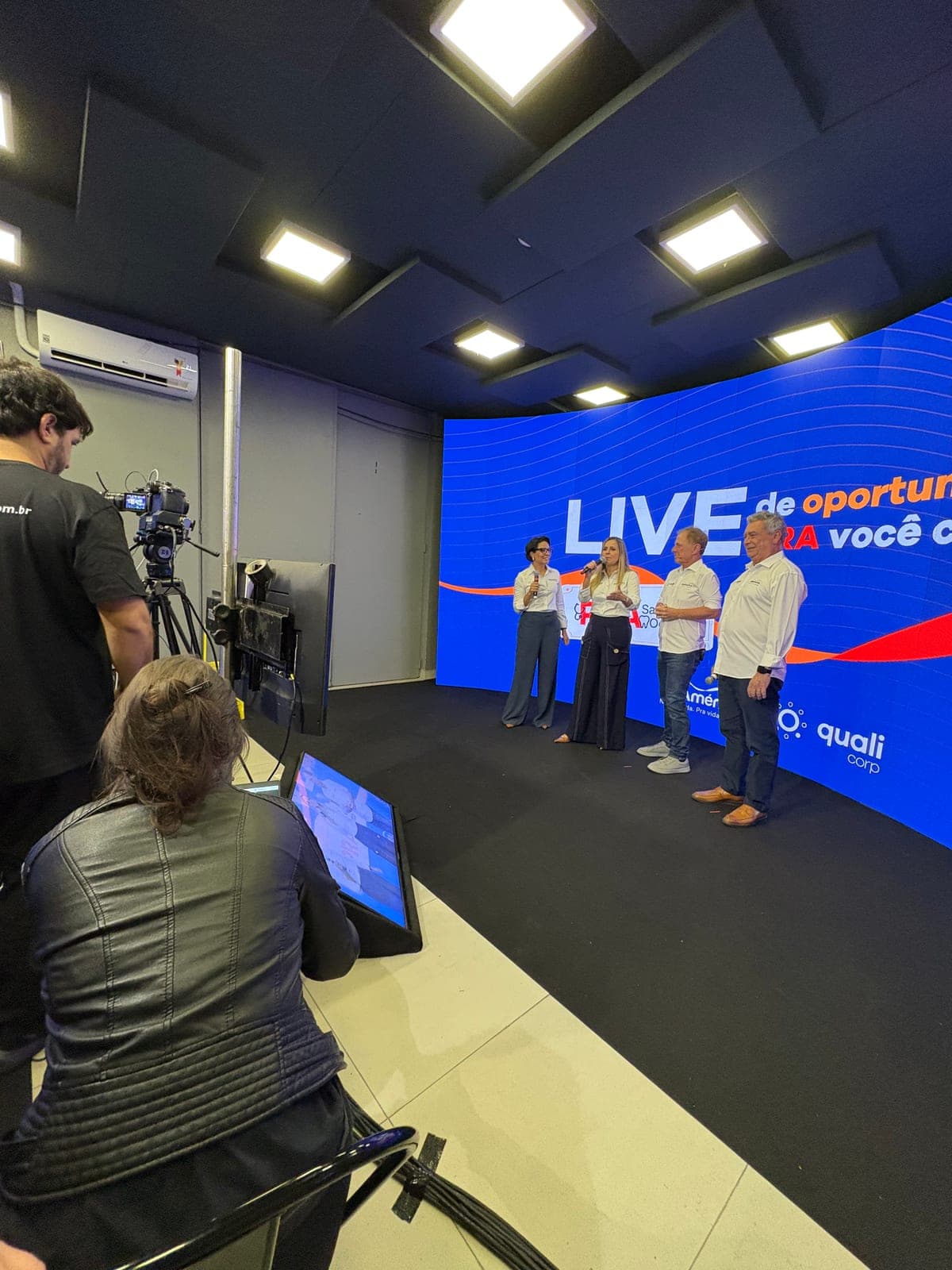 Operador de câmera enquadrando quatro apresentadores diante de uma parede curva de LED