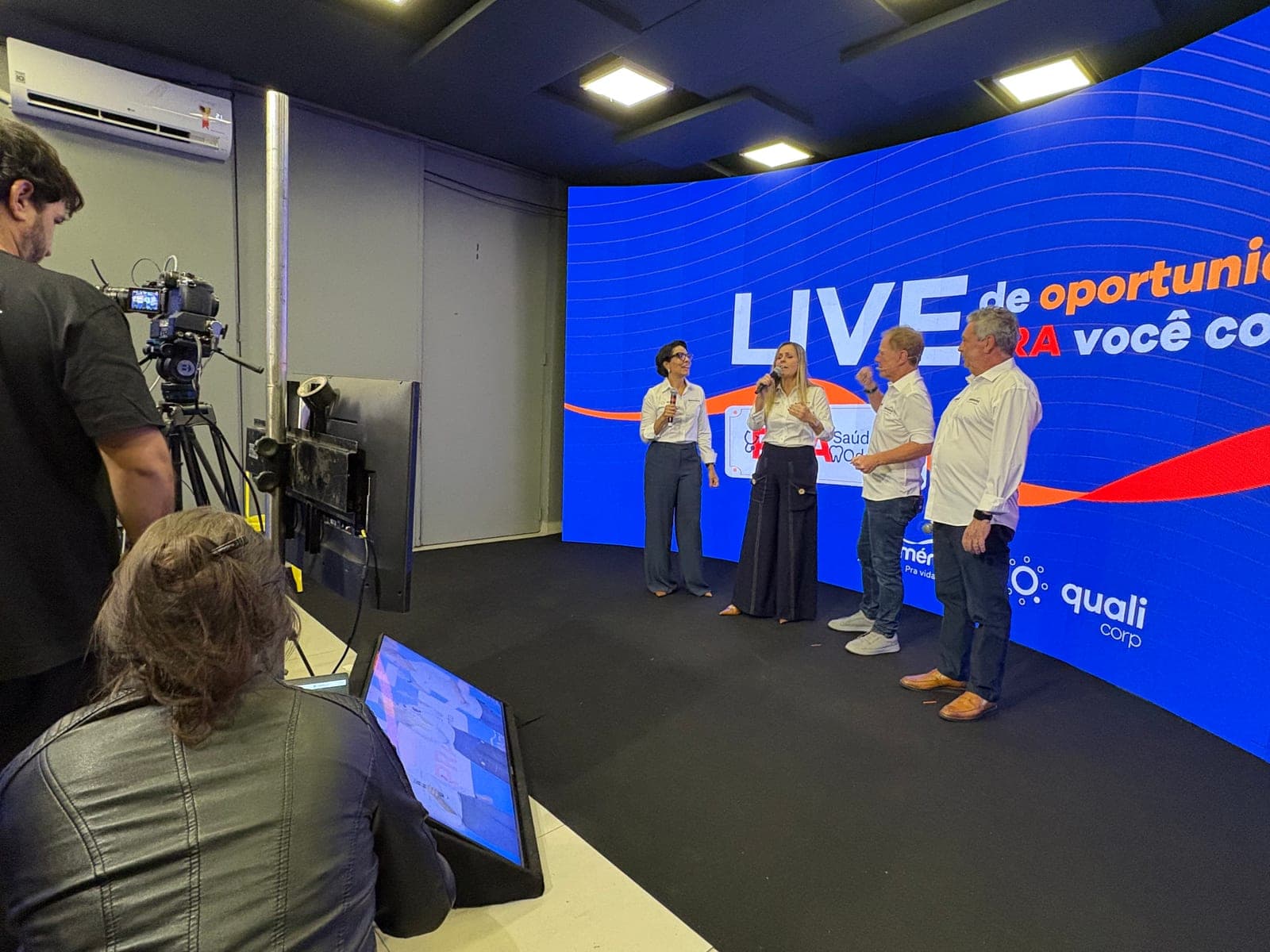 Live corporativa gravada no estúdio da Atmo, com quatro apresentadores diante do painel de LED curvo e o operador de câmera em primeiro plano