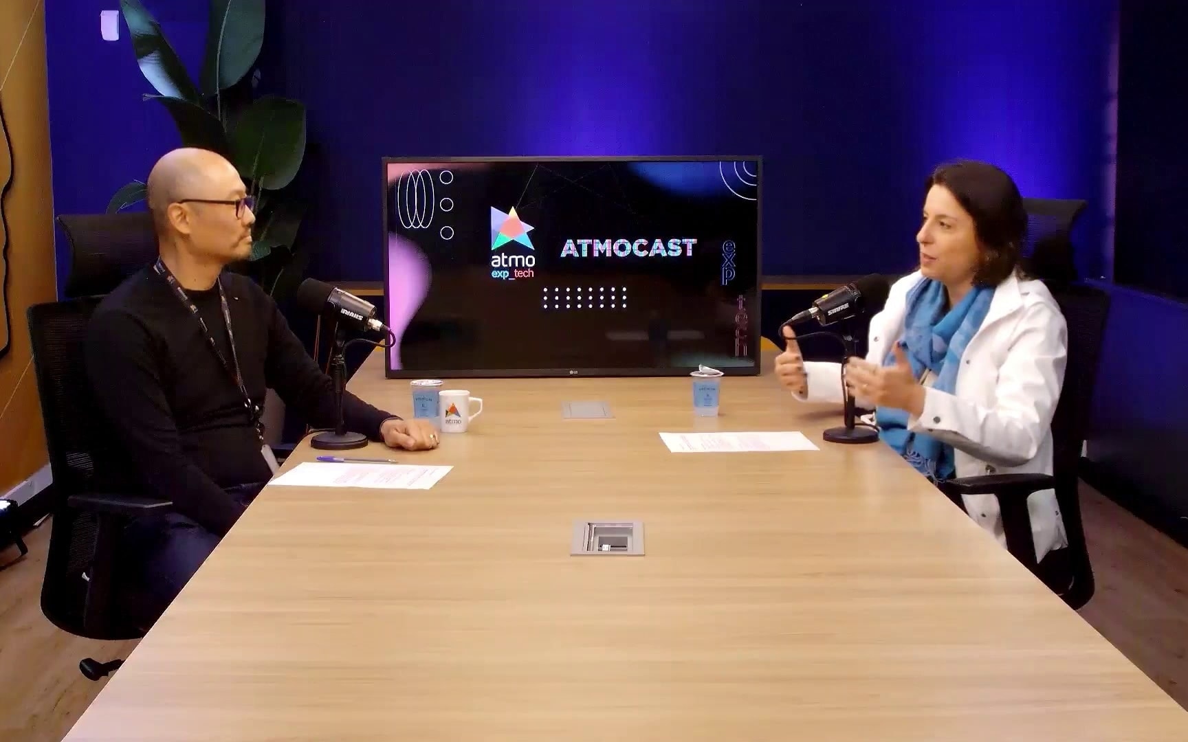 Gravação do Atmocast no estúdio da Atmo, com dois participantes à mesa, microfones de podcast e a tela do programa ao fundo